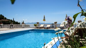 Una piscina d'aigua cristal·lina i blava, envoltada de gandules i sombrilles.