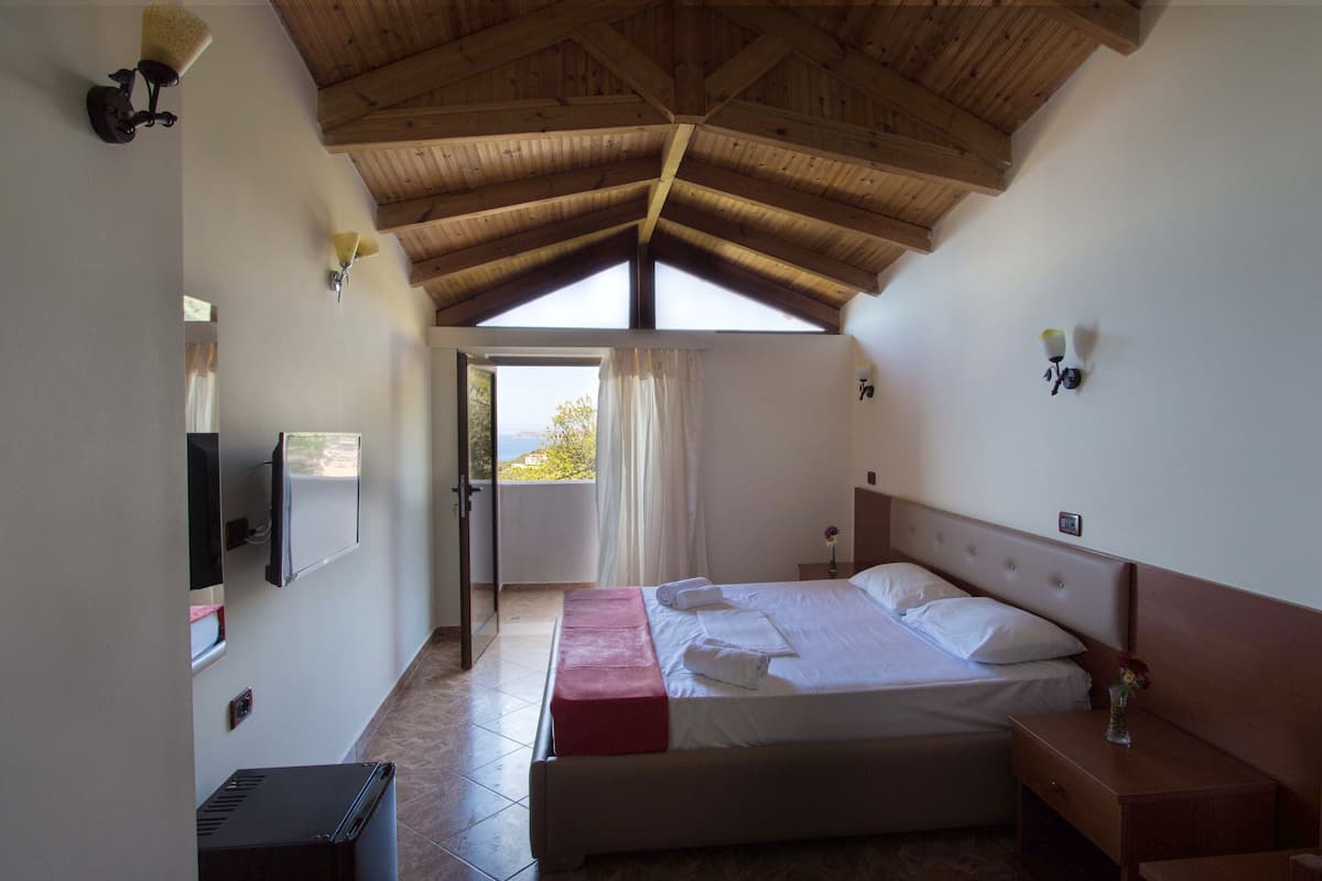 Een slaapkamer met een groot bed, een televisie, een houten plafond en uitzicht door een raam.