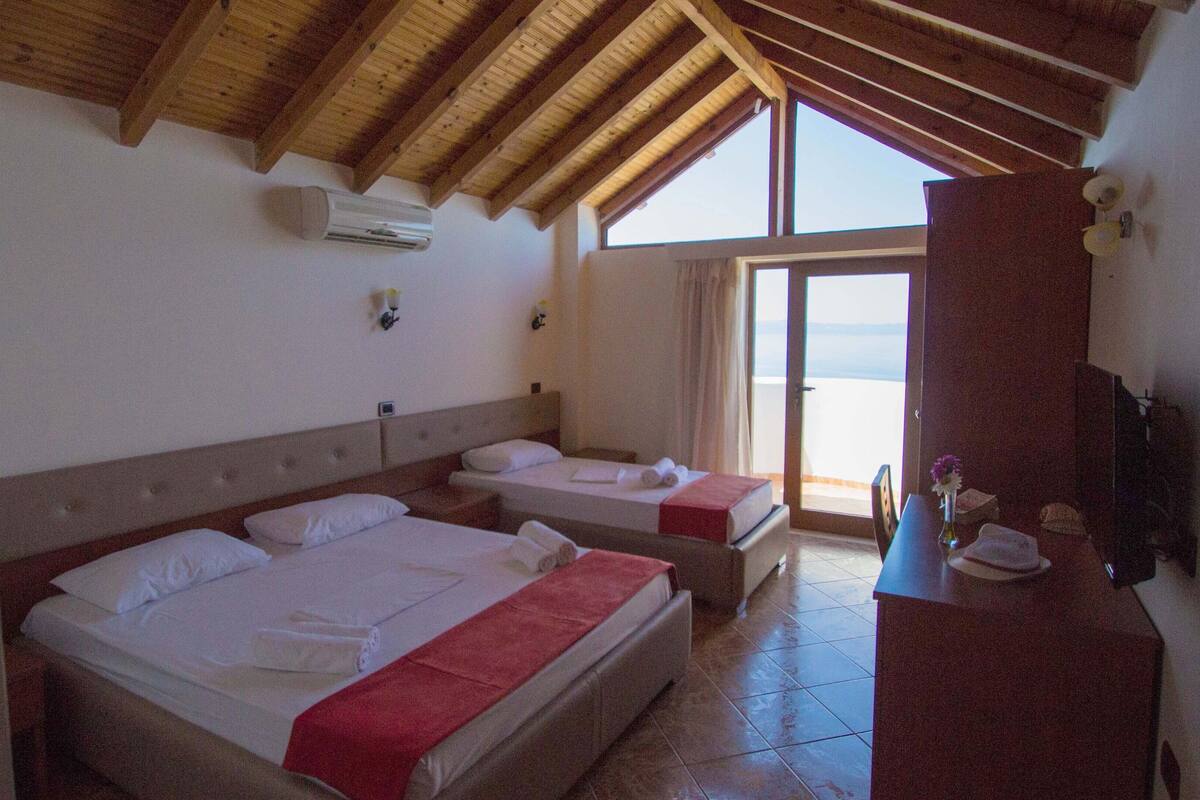 Een hotelkamer met twee bedden, een houten plafond, een groot raam en een bureau met een vaas.