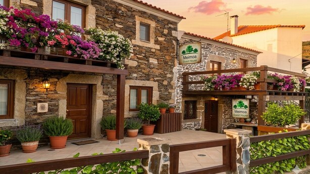 A stone building with a sign reading 'Meimoa Guest House,' potted plants, and a wooden fence. - Meimoa Guesthouse (Penamacor)
