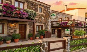 A stone building with a sign reading 'Meimoa Guest House,' potted plants, and a wooden fence. - Meimoa Guesthouse (Penamacor)