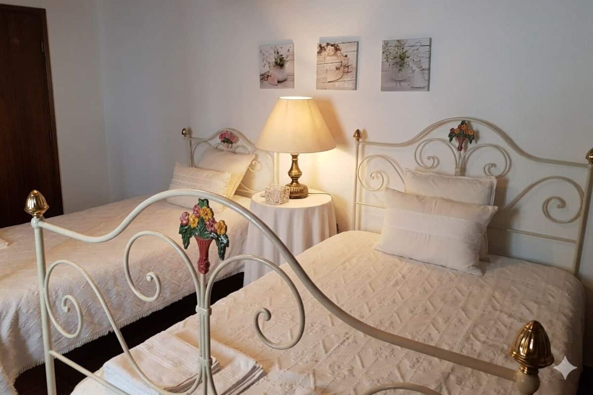 A bedroom with two beds, a bedside table with a lamp, and three wall-mounted pictures.