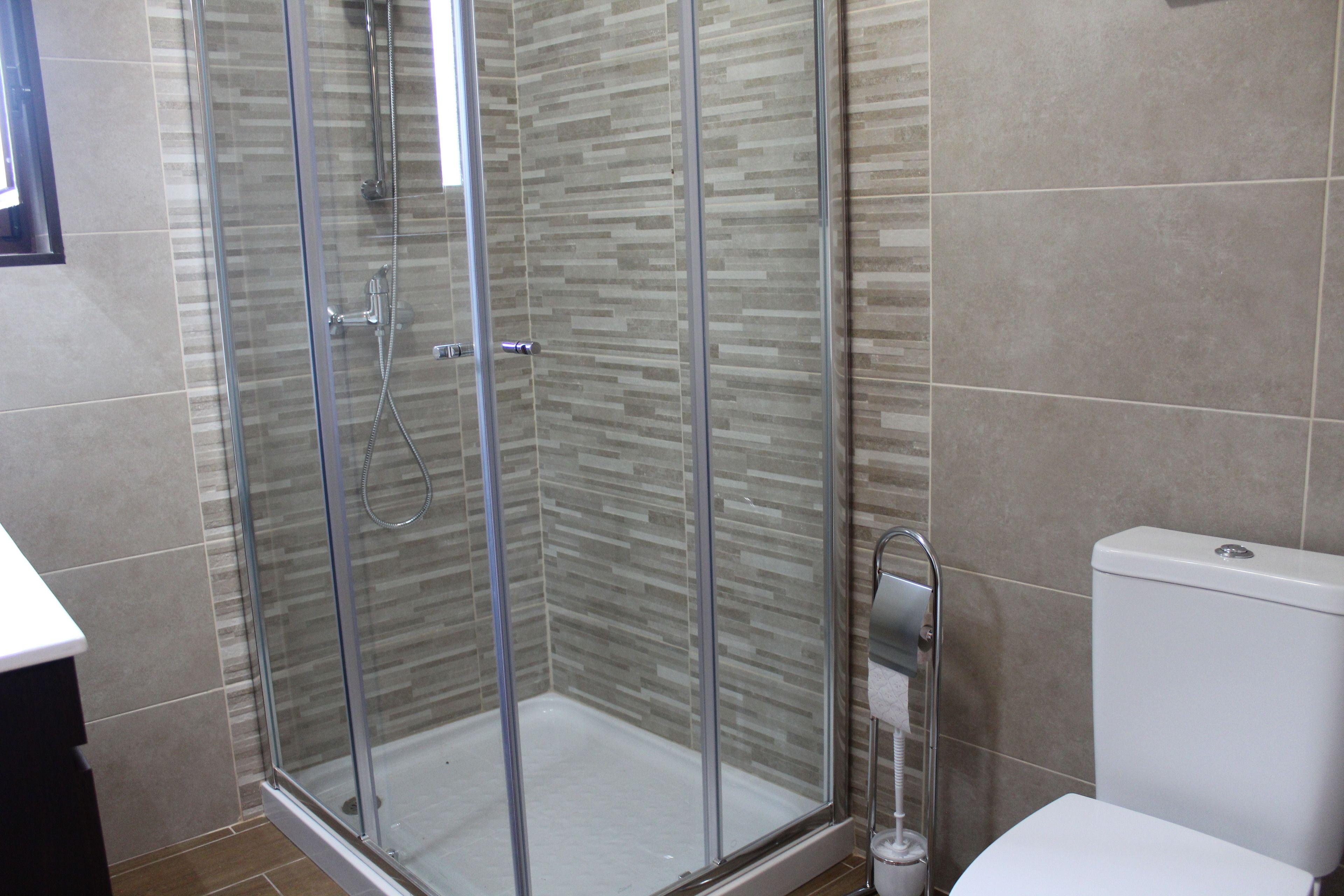 Un baño moderno con ducha de vidrio, inodoro blanco y suelo de baldosas.