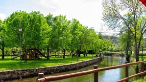 A riverside park with a wooden fence, stone wall, and picnic tables. - Meimoa Guesthouse (Penamacor)