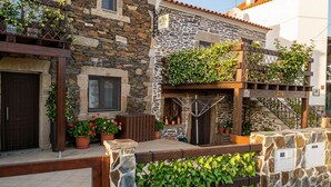 A stone building with a wooden balcony, potted plants, and a metal gate. - Meimoa Guesthouse (Penamacor)