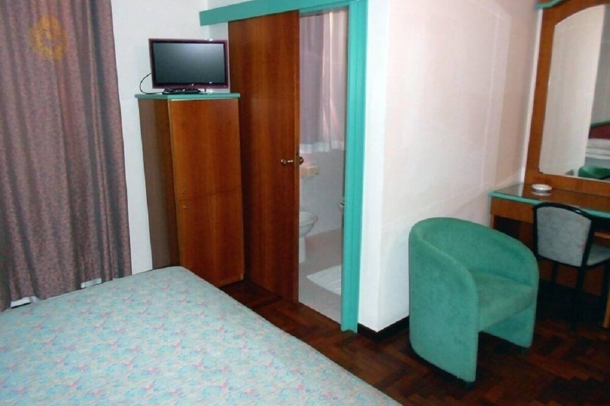 A bedroom with a bed, a desk, a chair, a television on a stand, and a wardrobe.
