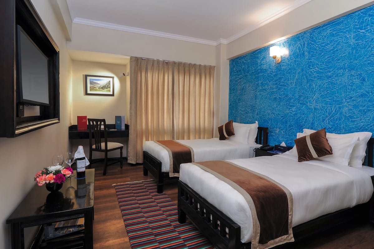 A hotel room with two beds, a desk, a chair, a TV, and a large window with curtains.