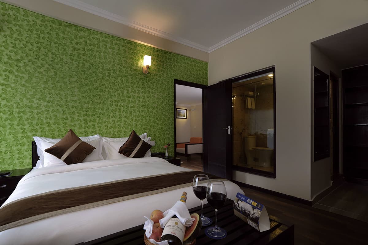 A hotel room with a bed, a nightstand, a tray with wine glasses, and a bottle of wine.