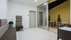 A modern interior with a sofa, a bench, a sliding glass door leading to an outdoor area with a table and chairs. - TH Collection Rooms (Oristano)