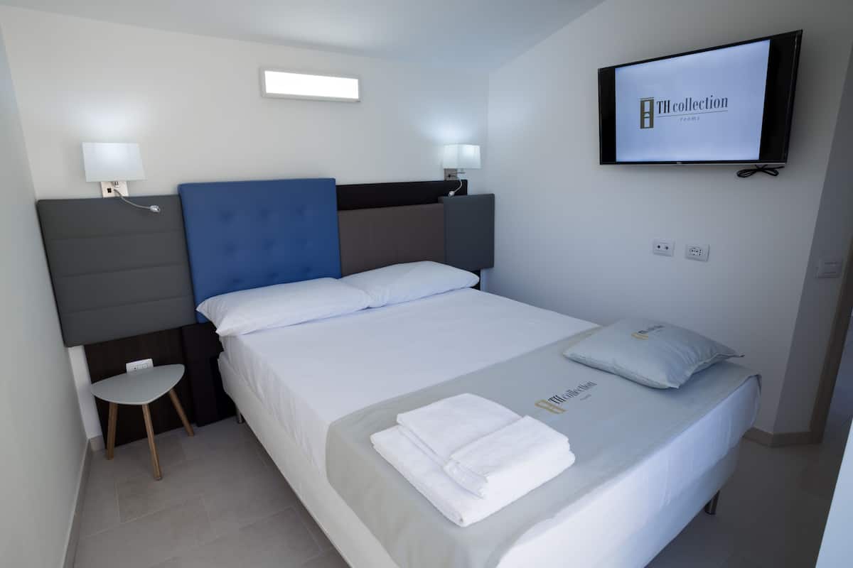 A hotel room with a bed, a TV mounted on the wall, and a small table with a lamp.
