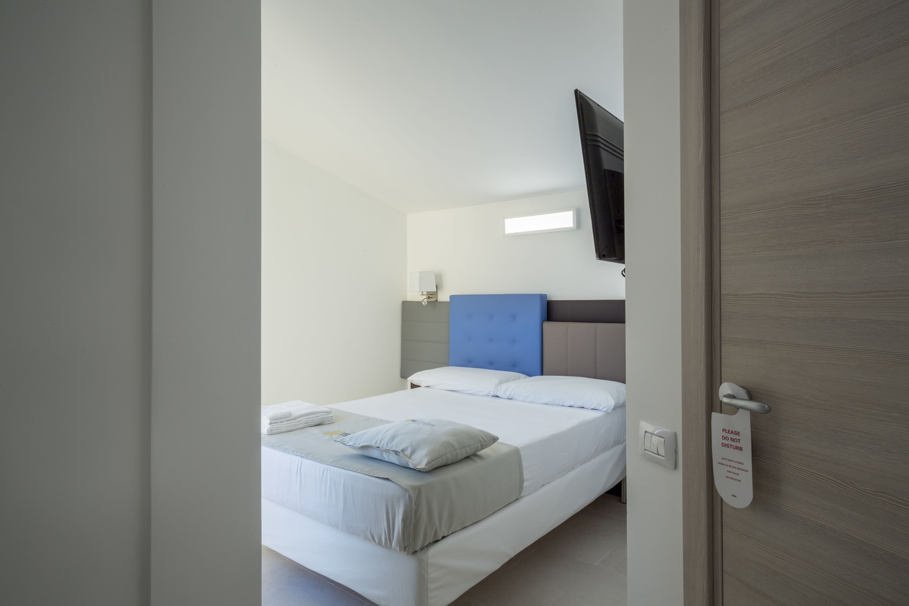 A hotel room with a bed, a flat-screen TV mounted on the wall, and a sign on the door.
