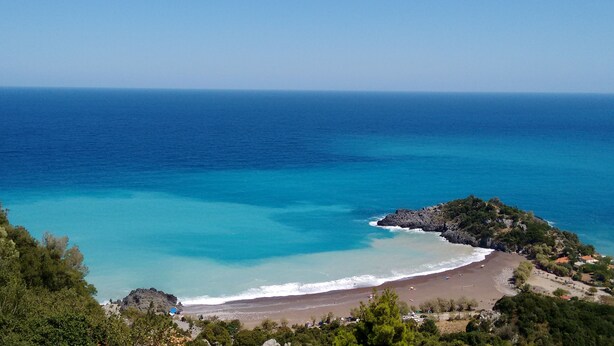 Paisagem costeira com praia, afloramentos rochosos e vegetação densa.