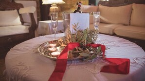 Uma mesa com arranjo de velas, uma garrafa e copos, numa sala com parede de pedra e um sofá.