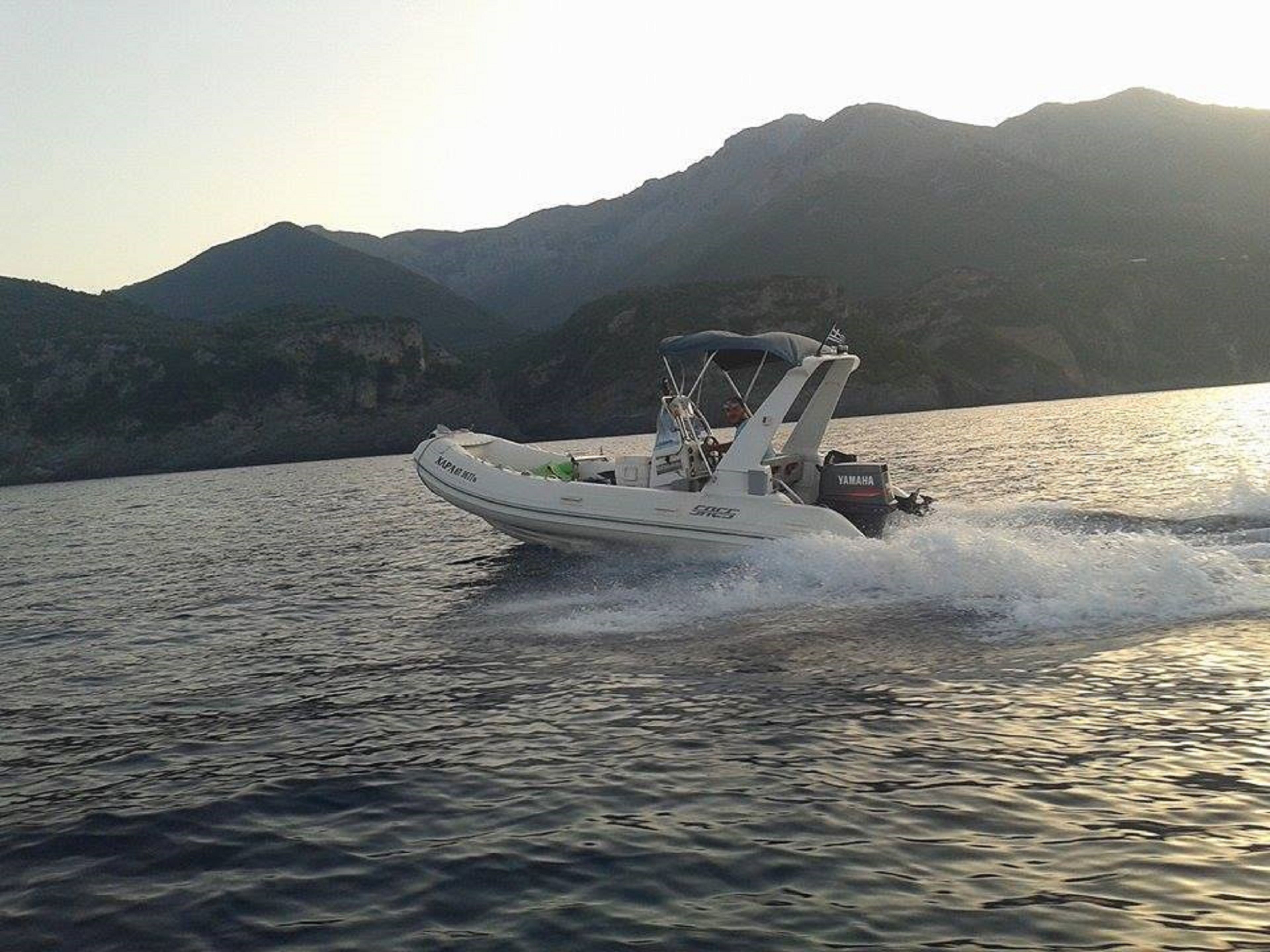 A small motorboat on calm water with mountains in the background.