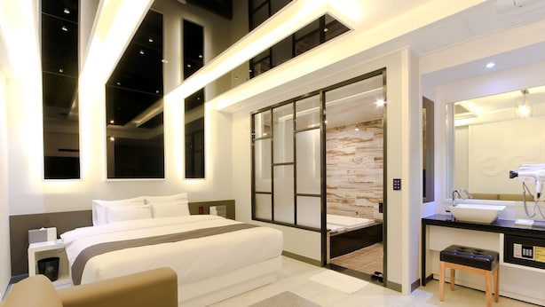 A modern hotel room with a large bed, a separate bathroom, a small seating area, and a large window. - G&G Hotel (Busan)