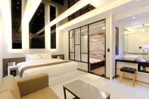 Une chambre d’hôtel moderne dotée d’un grand lit, d’une salle de bain séparée, d’un petit coin salon et d’une grande fenêtre.