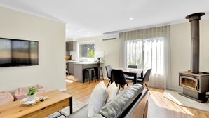 Een moderne woonkamer met een bank, een houten salontafel, een televisie, een open haard, een keuken en een eettafel.