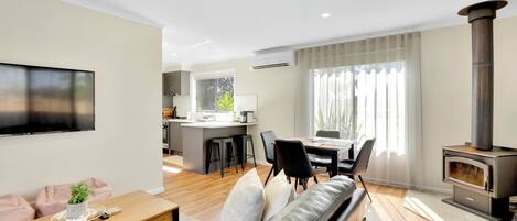 A modern living room with a sofa, a wooden coffee table, a TV, a fireplace, a kitchen area, and a dining table.