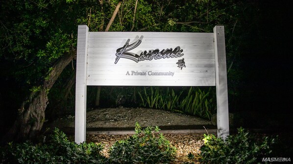 A wooden bench with a sign that reads "Kawanee A Private Community" surrounded by greenery.