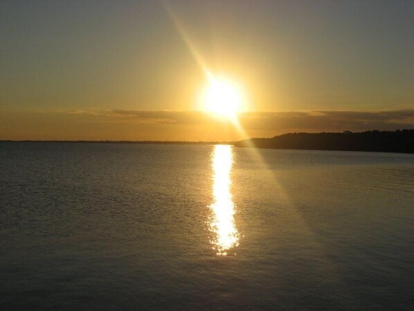 Ein Sonnenuntergang über ruhigem Gewässer mit einer entfernten Küstenlinie.