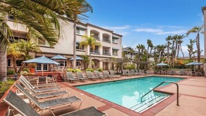 A pool area with lounge chairs, umbrellas, and a building with balconies. - Visit The Tamarack Beach Resort! Awesome Beach View! (Carlsbad)