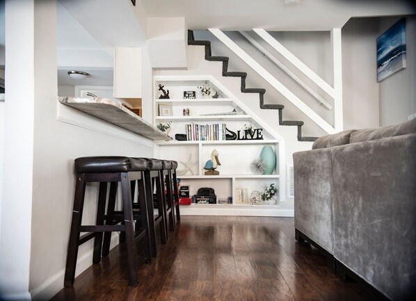 A modern living room with a grey sofa, a wooden coffee table, and a staircase with white railings. - OPEN FLOOR PLAN - One Block to Ocean, One Block to Bay (Beach Haven)