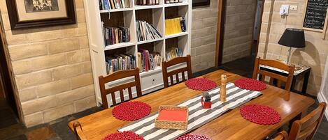 A dining area with a wooden table, red coasters, and a bookshelf filled with books and jars.