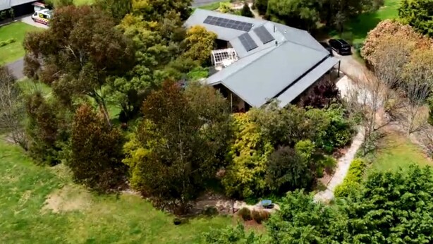 Une vue aérienne d’une maison avec un toit en pente, entourée d’une végétation luxuriante et d’arbres.