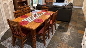 Un coin repas avec une table en bois, des sets de table rouges et un tapis à motifs.