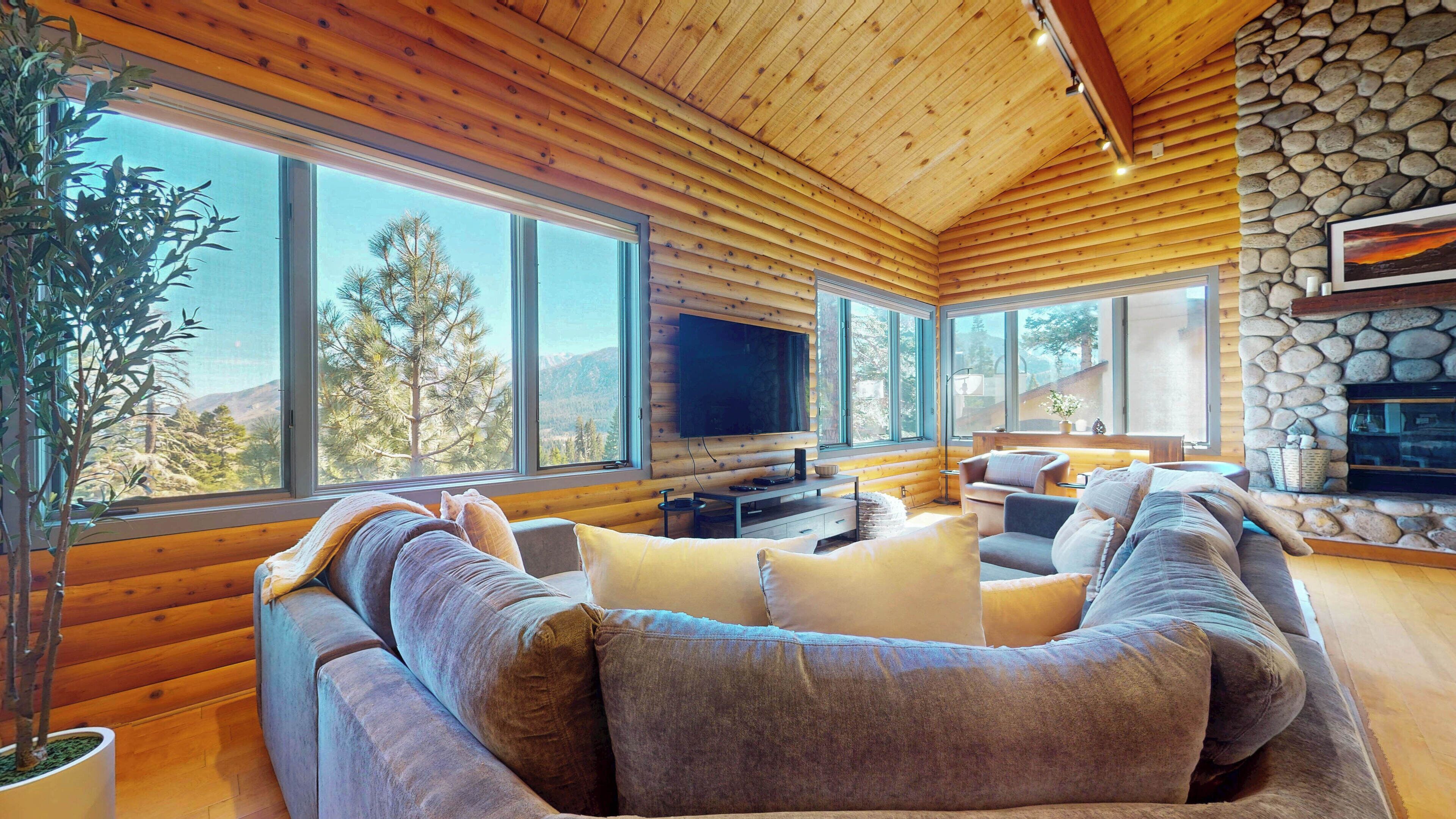A log cabin interior with a large sectional sofa, a flat-screen TV, and a stone fireplace.