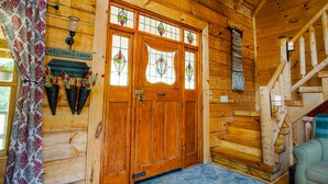 L’intérieur d’un chalet en bois, avec un escalier en bois, une pancarte de bienvenue et un sol en pierre.