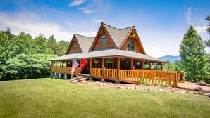 Une grande cabane en bois dotée d’un porche abrité et de nombreuses fenêtres, entourée d’une pelouse bien entretenue et d’arbres.