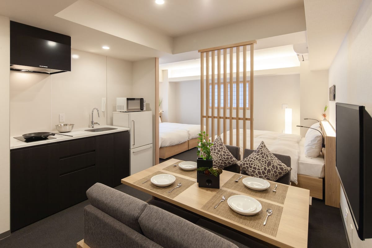A compact hotel room with a kitchenette, a dining area, a bed, and a TV.