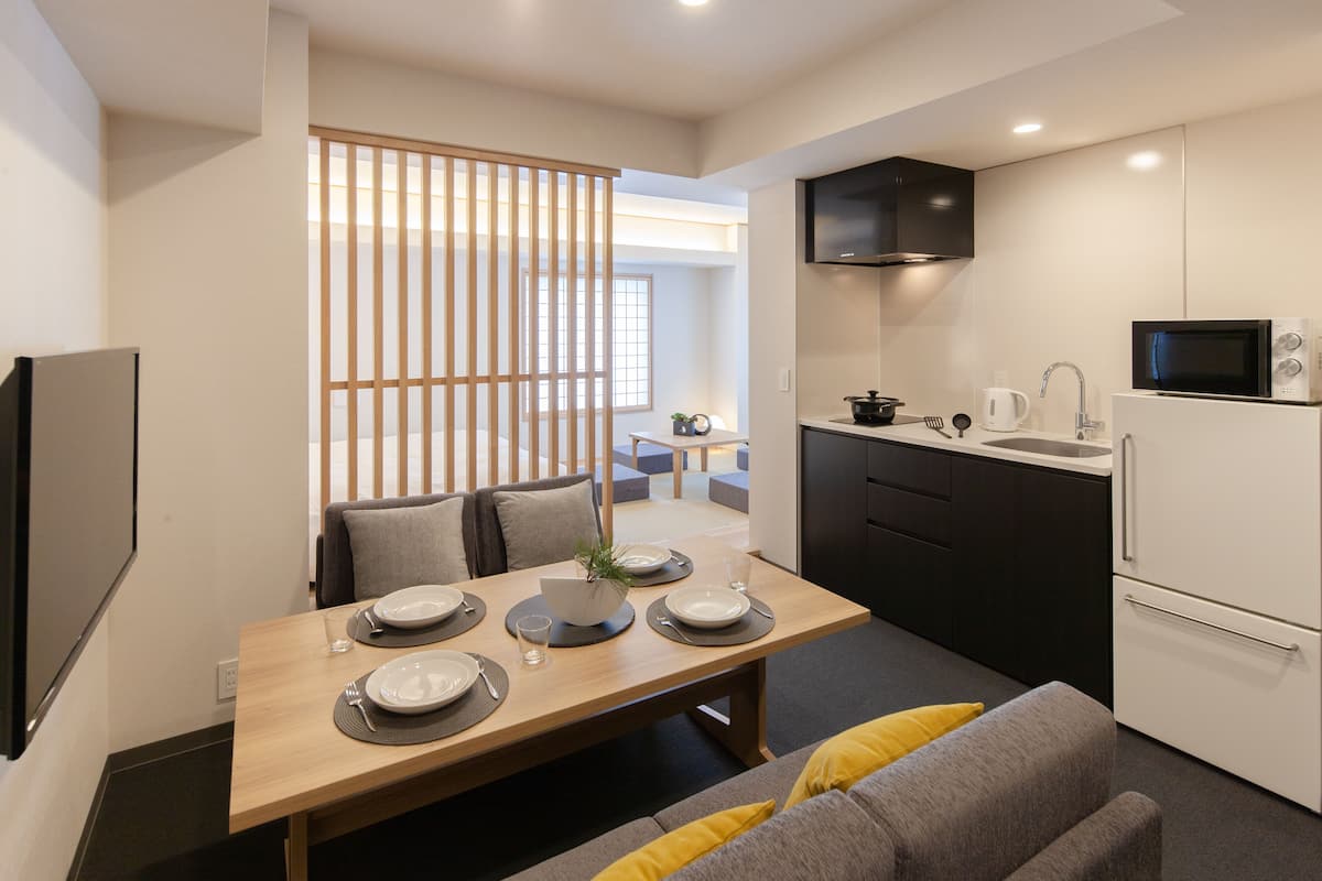 A modern kitchen with a microwave, stove, and sink. There is a dining area with a table set for two, and a sofa in the foreground.