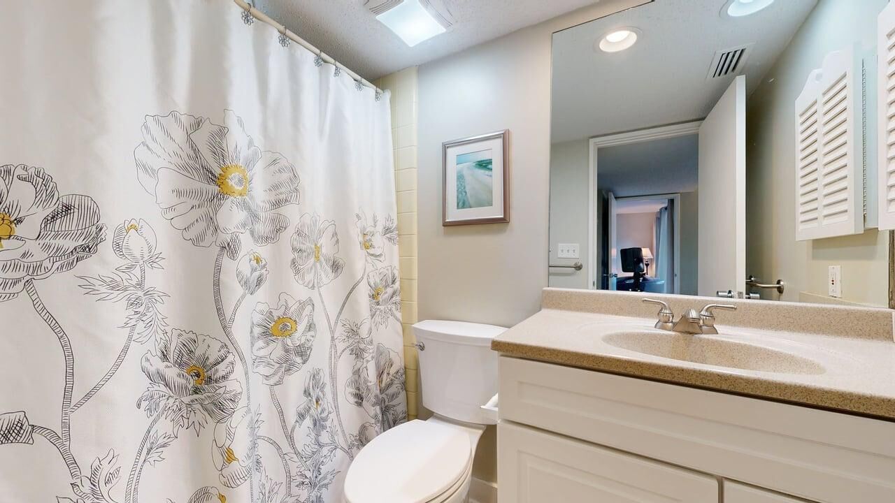 Un bagno con toilette, lavandino, specchio e tenda da doccia con motivi floreali.