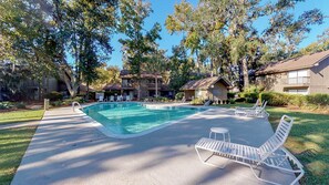 A swimming pool with lounge chairs, surrounded by trees and buildings.