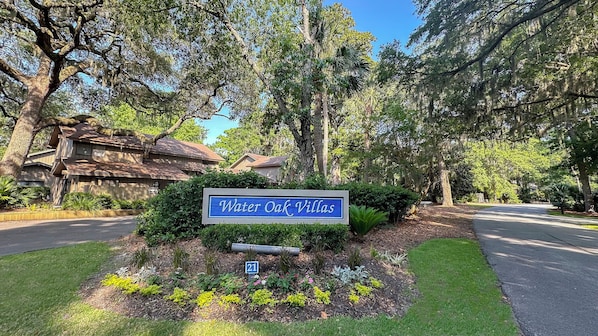 A sign for Water Oak Villas with a well-maintained garden and a road in the background.