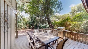 An outdoor deck with a table and chairs, surrounded by lush greenery and trees.
