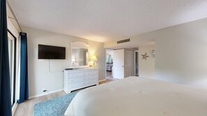 A bedroom with a bed, dresser, mirror, and a television on the wall.