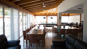 Un comedor amplio con una larga mesa y varias sillas, ventanas grandes y un ventilador de techo.