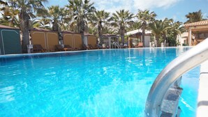 Una piscina con agua azul cristalina, rodeada de palmeras y sillas de descanso.
