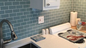 Una cocina con salpicadero de azulejos azules, pileta de acero inoxidable, armarios blancos y encimera blanca.