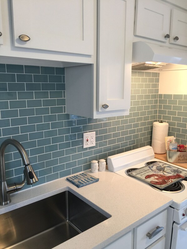 Una cocina con salpicadero de azulejos azules, pileta de acero inoxidable, armarios blancos y encimera blanca.