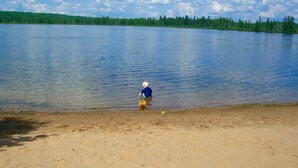 A lake with a sandy shore and a person in a blue shirt playing with a yellow bucket.