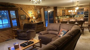 A cozy living room with a brown leather sofa, a wooden coffee table, and a dining area with a chandelier.