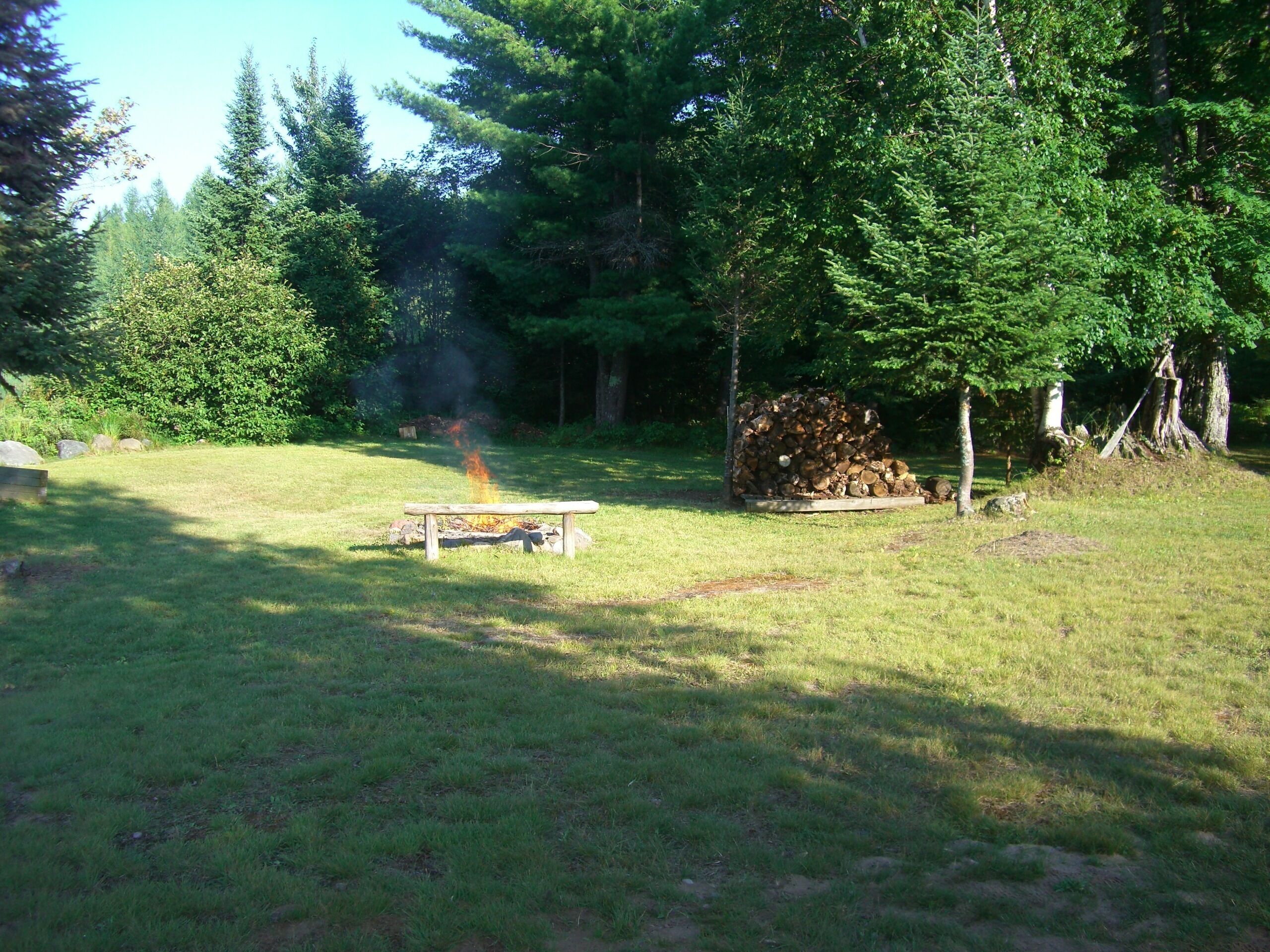 A grassy outdoor area with a fire pit and a stack of firewood.