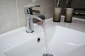 Ein Waschbecken mit fließendem Wasser, eine Seifenspender und ein Spiegel.