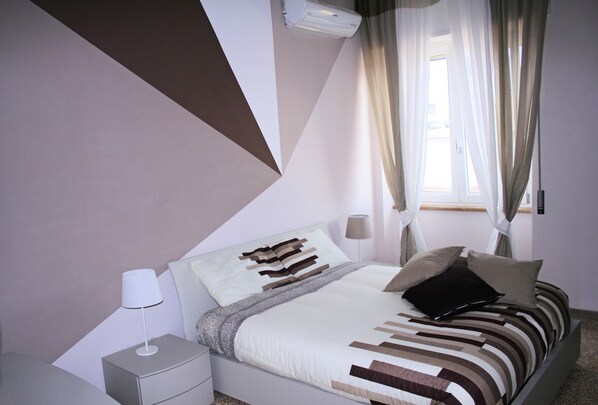 Ein Schlafzimmer mit Bett, Nachttisch, Lampe und Vorhängen.