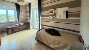 Ein Hotelzimmer mit zwei Betten, einem großen Fenster, einem Deckenventilator und einer Wandklimaanlage.