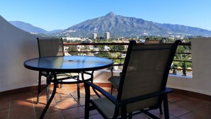Ein Balkon mit Tisch und Stühlen, der Blick auf Berge und Stadt bietet.